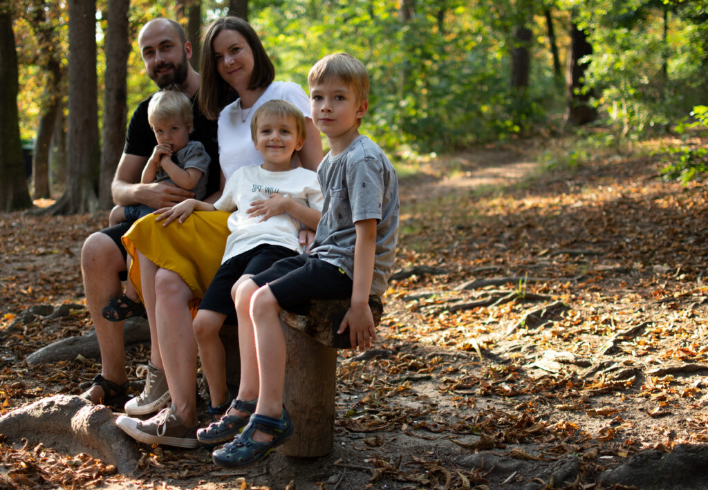 rodina se třema klukama sedí na lesní lavičce v lese